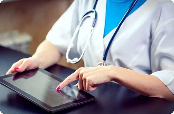 Uma médica vestida de branco, sentada com os braços apoiados na mesa, segurando um tablet e um estetoscópio em volta do pescoço.